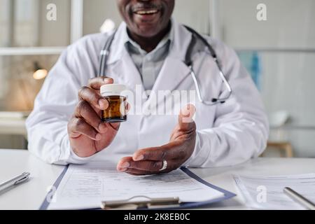 Primo piano del pediatra africano in camice bianco che prescrive la medicina al paziente seduto al tavolo in ufficio Foto Stock