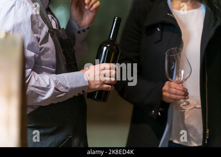 Le mani versano vino rosso da una bottiglia in un bicchiere in autentiche cantine Foto Stock
