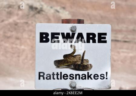 Attenzione bianca ai rattlesnakes segno su un sentiero escursionistico nei badlands. Foto Stock