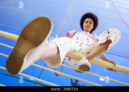 Donna nera seduta sulla recinzione vicino all'edificio Foto Stock