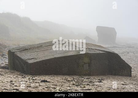 Vecchie fortificazioni costiere tedesche marciate su una spiaggia nella nebbia mattutina Foto Stock