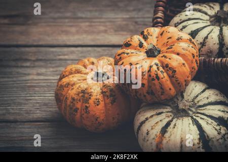 Diverse piccole zucche su un asse di legno e in un cesto Foto Stock