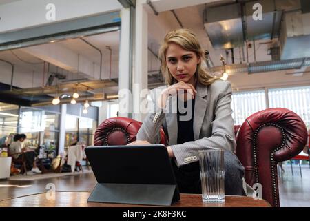 Giovane donna seduta in poltrona che lavora su un tablet digitale Foto Stock