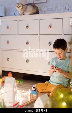 Ragazzo che gioca con il trenino giocattolo di fronte al mobile bianco a casa Foto Stock