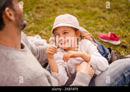 Ragazza sorridente che guarda il padre seduto sull'erba Foto Stock