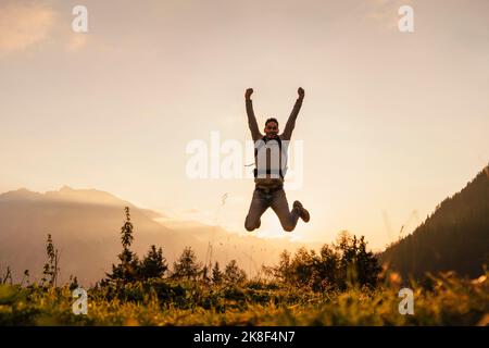 Uomo felice che salta in cima alla montagna al tramonto Foto Stock