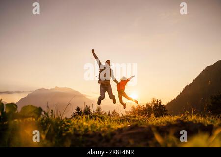 Felice uomo con figlia che salta in cima alla montagna Foto Stock