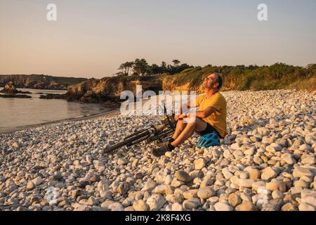 Uomo maturo che riposa in bicicletta sulla riva al tramonto Foto Stock