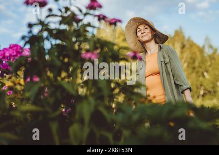 Donna sorridente con cappello giorno sognando in giardino Foto Stock