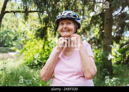 Senior sorridente donna che indossa il casco in bicicletta nel parco Foto Stock