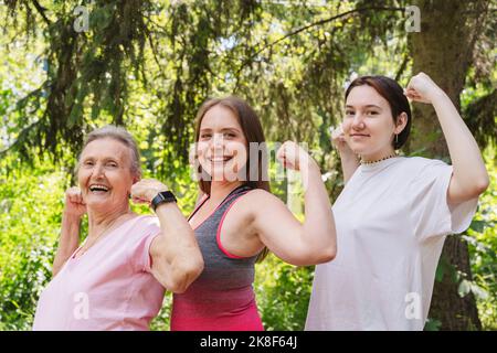 Donna anziana attiva che flette i muscoli con la figlia e la nipote al parco Foto Stock