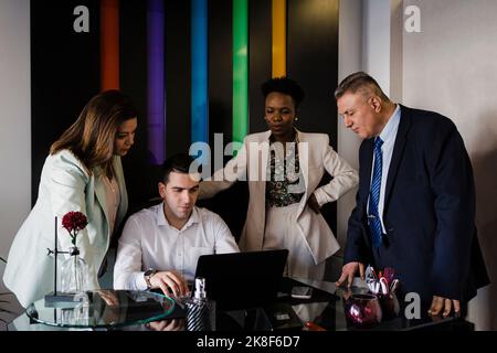 Giovane uomo d'affari con i colleghi che discutono sul laptop in ufficio Foto Stock