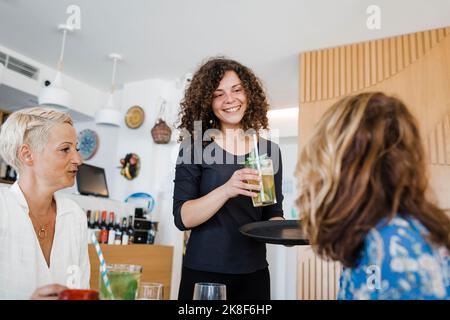 Cameriera giovane e felice che serve cocktail ai clienti al ristorante Foto Stock