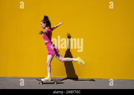 Donna con le braccia in equilibrio su skateboard di fronte al muro Foto Stock