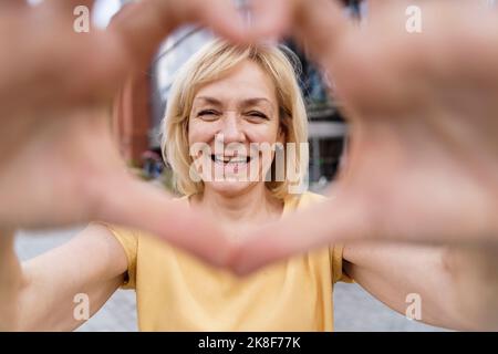 Donna felice che fa il cuore forma con le mani Foto Stock