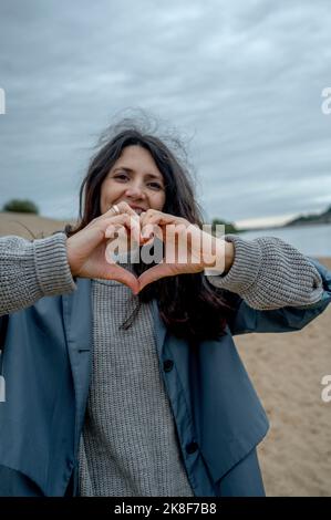 Donna sorridente che forma il cuore con le mani Foto Stock