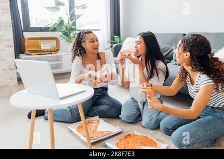 Gli amici mangiano la pizza godendosi insieme nel soggiorno Foto Stock