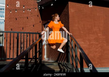 Donna in abito arancione bilanciamento su ringhiere di scala Foto Stock