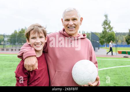 Uomo anziano sorridente che tiene la sfera di calcio con il braccio intorno al nipote Foto Stock