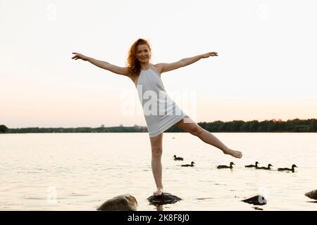 Donna sorridente con le braccia distese sulla roccia al tramonto Foto Stock