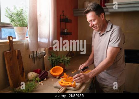 Uomo maturo sorridente che taglia la zucca a bordo in cucina Foto Stock