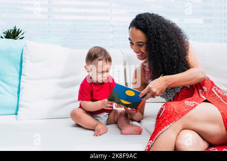 Felice madre che legge il libro di storia a figlio seduto sul divano a casa Foto Stock