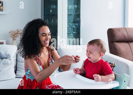 Madre felice con bambino piangente seduto in seggiolone a casa Foto Stock