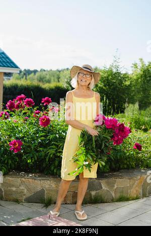 Donna con mazzo di fiori in piedi vicino alle piante in giardino Foto Stock