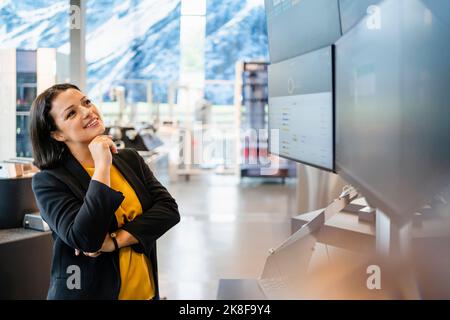 Donna d'affari matura sorridente con mano sul mento guardando il monitor del computer Foto Stock