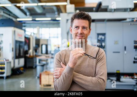 Sorridente uomo d'affari premuroso che tiene gli occhiali nell'industria Foto Stock
