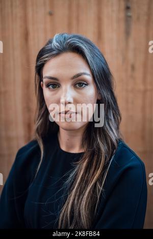 Giovane donna fiduciosa con capelli lunghi davanti al muro Foto Stock