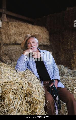 Contadino anziano seduto su pagliaio in fattoria Foto Stock