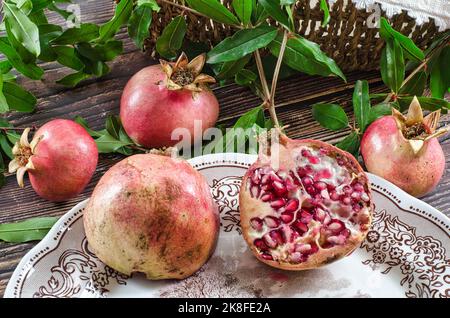 gruppo di melograni su un tavolo rustico in legno. Melograno tagliato in due parti all'interno di un piatto d'annata Foto Stock