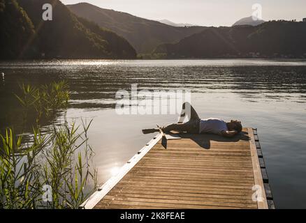 Uomo maturo che si rilassa con un computer portatile sul molo sul lago Foto Stock