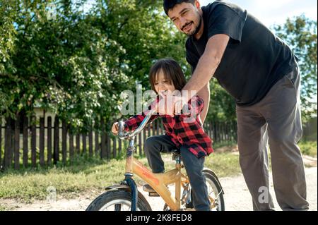 Uomo che spinge il figlio in bicicletta Foto Stock