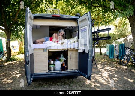 Donna anziana sdraiata nel libro di lettura del camper van Foto Stock