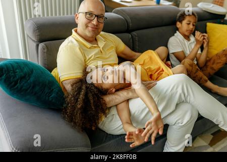 Ragazza sdraiata sul grembo del padre da fratello sul divano a casa Foto Stock