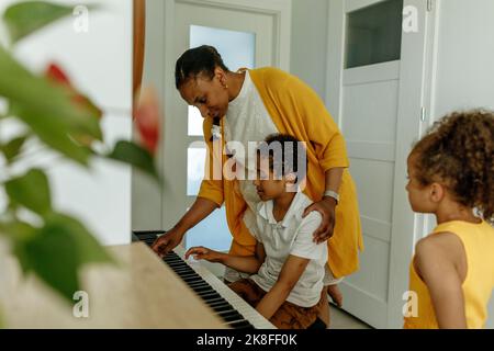 Ragazza che guarda la madre che insegna al figlio di suonare il pianoforte a casa Foto Stock