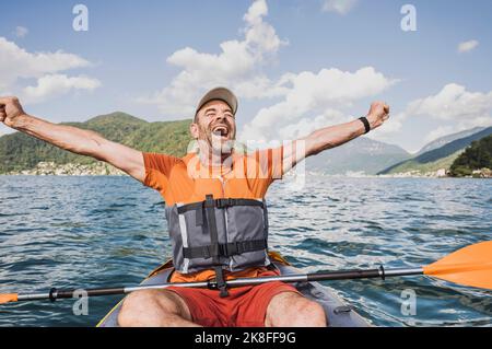 Uomo maturo eccitato urlando con le braccia distese sul lago Foto Stock