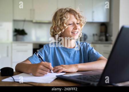 Ragazzo felice che fa i compiti a casa guardando il notebook Foto Stock