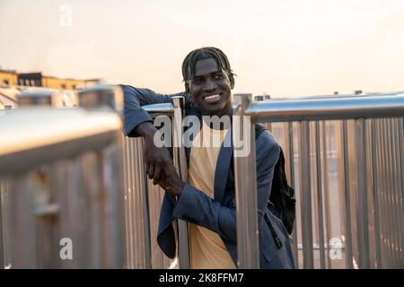 Giovane uomo d'affari sorridente in piedi accanto alle ringhiere Foto Stock