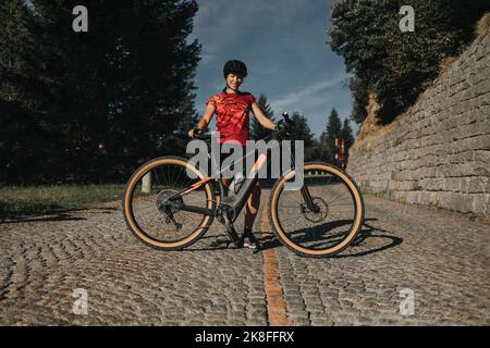 Donna sorridente con la bicicletta in piedi su strada acciottolata Foto Stock