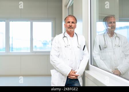 Medico anziano che si appoggia sulla finestra di vetro Foto Stock