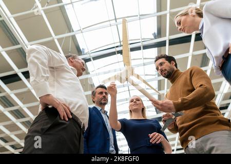 Donna d'affari sorridente con i colleghi che discutono sul modello delle turbine eoliche nell'industria Foto Stock