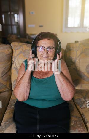 Buona donna anziana che si diverti con la musica con le cuffie a casa Foto Stock