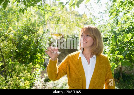 Donna matura sorridente che tiene un bicchiere di vino bianco in giardino Foto Stock
