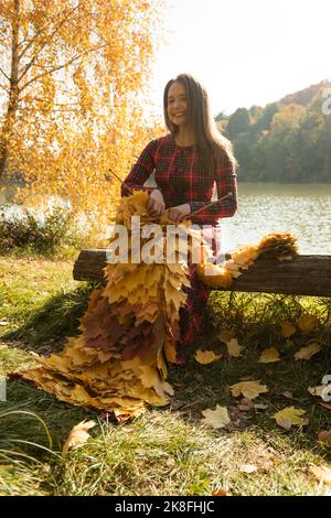 Donna sorridente sciarpa a maglia con foglie d'acero nel parco Foto Stock