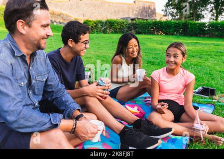 Famiglia multirazziale gustando un drink in prato al picnic Foto Stock