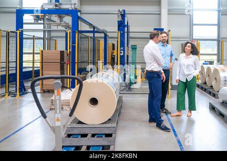 Donna d'affari in piedi con mano in tasca discutere con i colleghi del settore Foto Stock