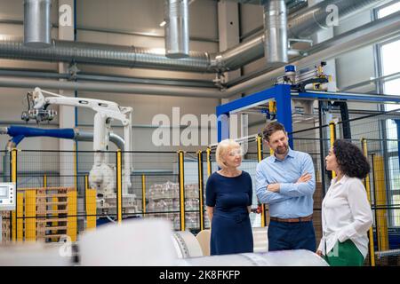Donna d'affari in piedi con mano in tasca discutere con i colleghi del settore Foto Stock